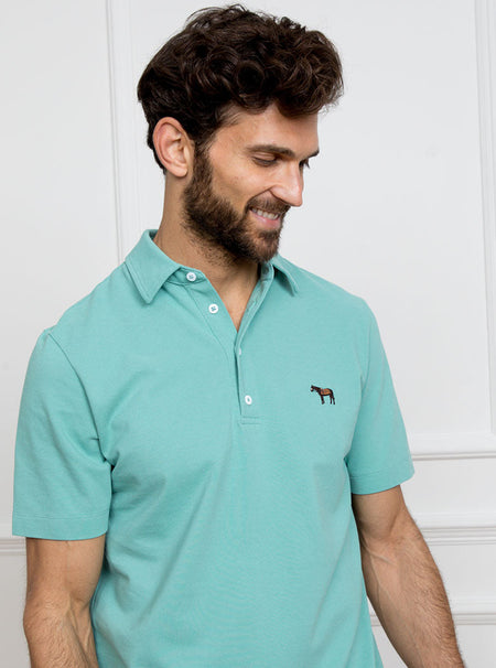 Man wearing avocado green polo shirt in 100% cotton with Newmarket 875 horse logo embroidered on the front.